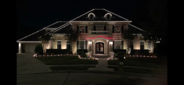 Two-story home with warm white roofline lights, red accent lighting, and wreaths at night